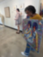 Victoria Seals shows her quilt depicting herself and her sister. Behind, Sam Moore stands by her Affluence series
